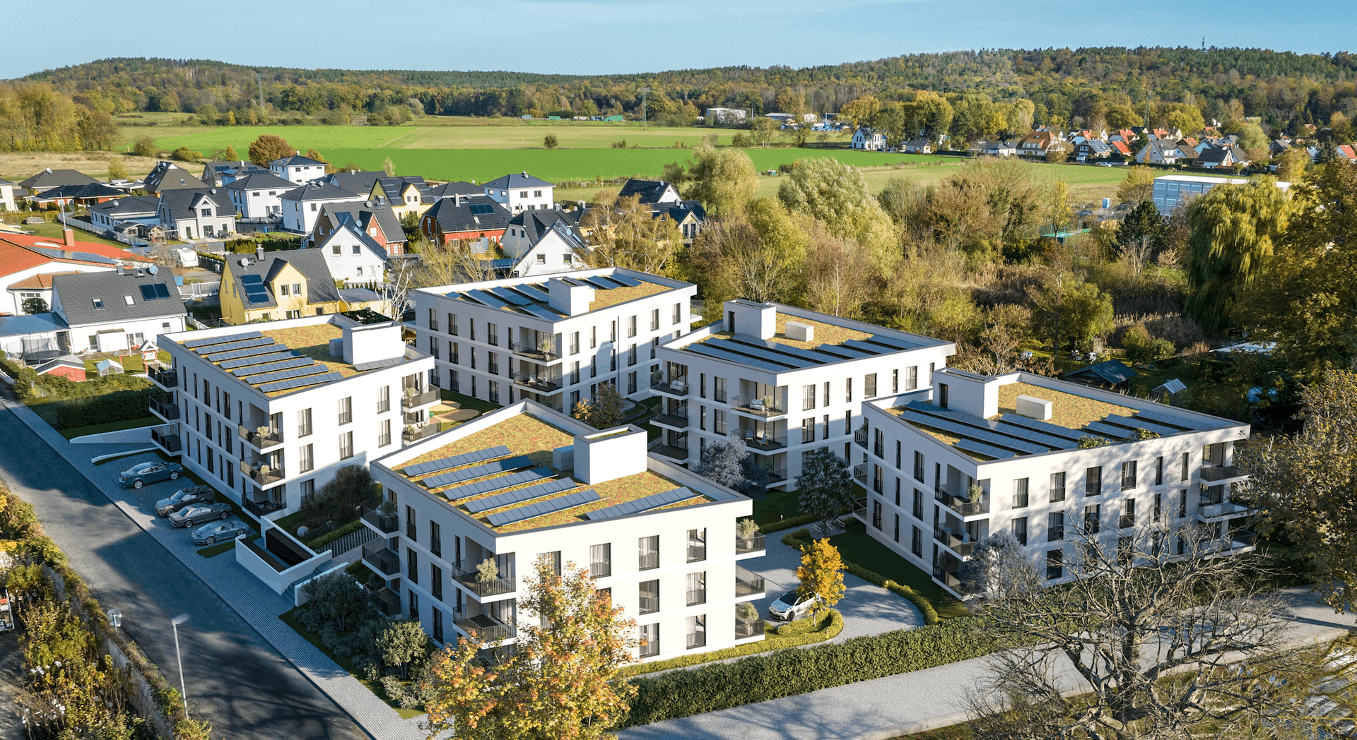 Fotorealistische 3D-Architekturvisualisierung eines modernen Neubauquartiers aus der Vogelperspektive. Die detaillierte Luftaufnahme zeigt ein geplantes Wohnprojekt mit mehreren weißen Mehrfamilienhäusern, die mit nachhaltigen Gründächern und Photovoltaikanlagen ausgestattet sind. Moderne Balkone, großzügige Fensterfronten und ansprechende Außenanlagen mit Parkplätzen runden das Architekturkonzept ab. Die Gebäude fügen sich harmonisch in die umliegende grüne Vorstadtlandschaft ein – ein ideales Bild für die professionelle Immobilienvermarktung und Projektentwicklung.